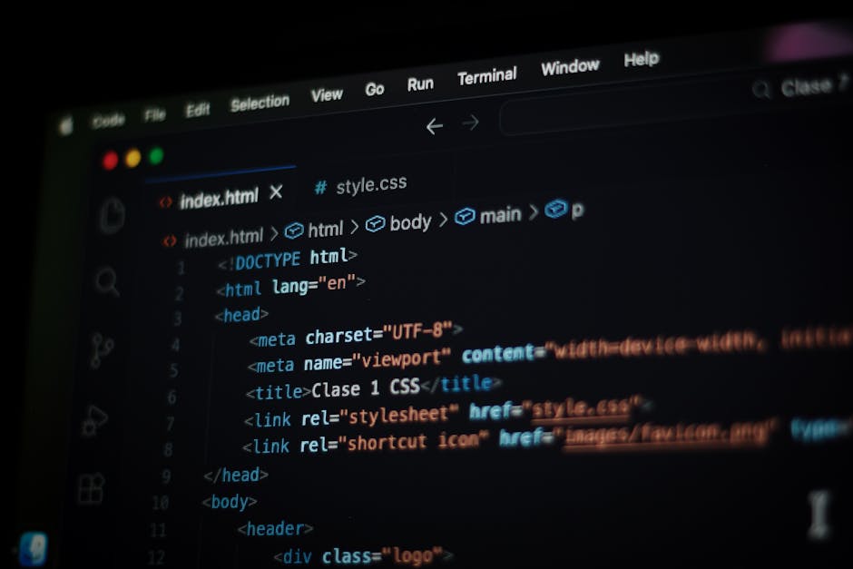 A close-up view of a person's hand operating a silver laptop on a wooden desk, with the screen displaying lines of colorful programming code. The person's wristwatch is partially visible on their left